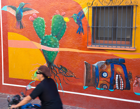 Xochimilco, Oaxaca, Mexico: A motorcyclist rides past a vibrant mural; the neighborhood  near downtown Oaxaca is known for its many murals.