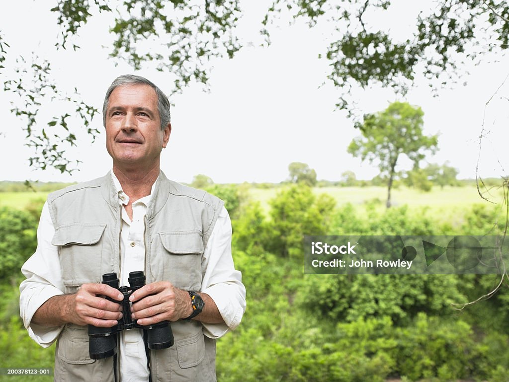 Senior hombre en safari, sonriente sosteniendo binoculares - Foto de stock de Hombres libre de derechos