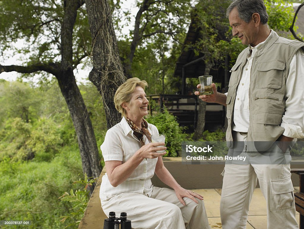 Casal maduro depois de bebidas no terraço no lodge, sorrindo - Foto de stock de Alta Sociedade royalty-free