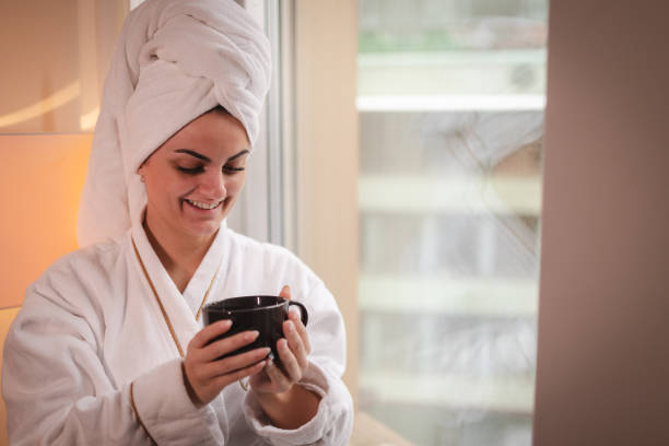 istock Beautiful young woman drinking coffee while looking out the hotel room window 2003805632