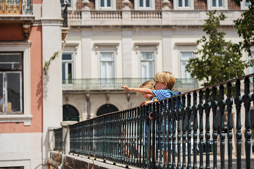 Young travelers, boy and girl at Lisbon viewpoint pointing with fingers, Portugal architecture on background