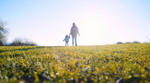 Baby girl learning to walk with mother in nature at sunset. Teaching children about sustainability.