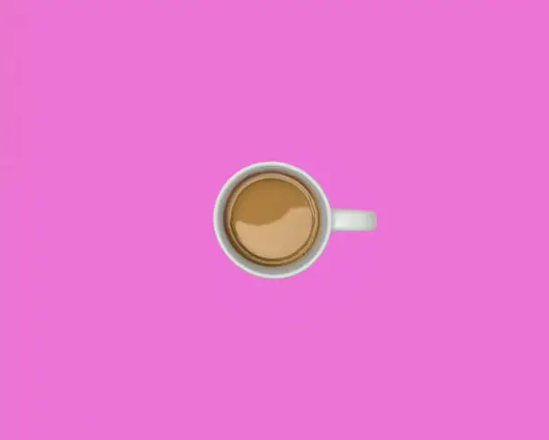 Overhead view of a cup of coffee with cream on a solid pink background with copy space