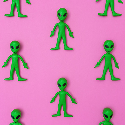 Green alien toy dolls in a repeating pattern on a solid pink background