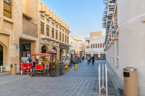 Outdoor sidewalk cafes and colorful shops at dusk in the historic Souq Waqif market in the historic center of Doha Qatar. Souq Waqif is a marketplace in Doha, in the state of Qatar. The souq sells traditional garments, spices, handicrafts, and souvenirs. It is also home to restaurants and shisha lounges. The original building dates back to the late 19th to early 20th centuries in a traditional Qatari architectural style.