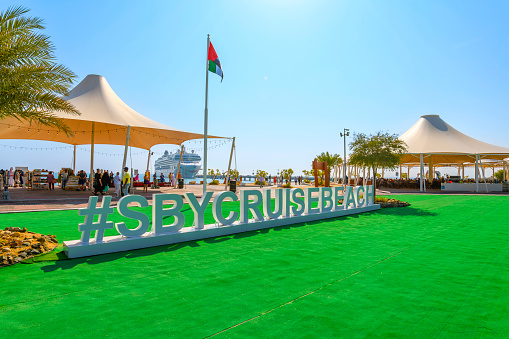 The hashtag welcome sign, cruise ship, and tourist tents selling souvenirs, on Sir Bani Yas Island, a wildlife sanctuary and resort in the United Arab Emirates. Sir Bani Yas Island is part of the Al Gharbia region of the United Arab Emirates. It's dominated by the Arabian Wildlife Park, with its roaming giraffes, cheetahs and gazelles. Multiple archaeological sites across the island include the ruins of an ancient Christian monastery. Salt dome hills define the island’s desert interior. The coast features beaches, sea kayak routes and a shipwreck.