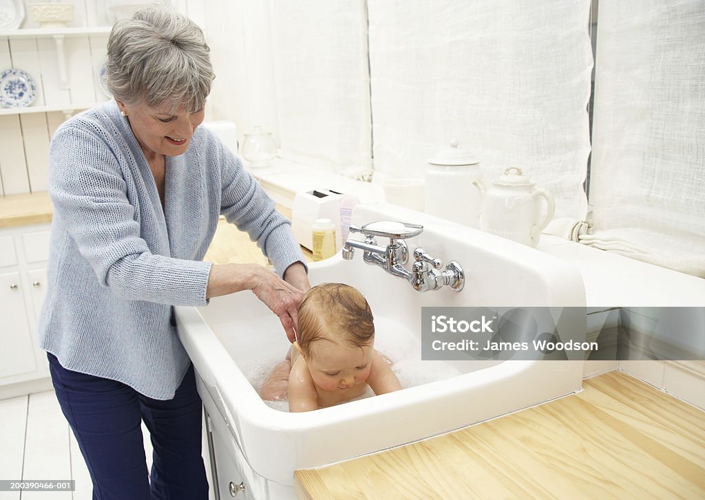 Petite-fille de Grand-mère baignant bébé (8 à 10 mois) dans un évier, sm - Photo de Bébé libre de droits