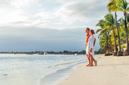 Couple in love hugging on sandy exotic beach while having evening walk by Trou-aux-Biches seashore on Mauritius island enjoying sunset. People relationship and tropic honeymoon vacations concept image