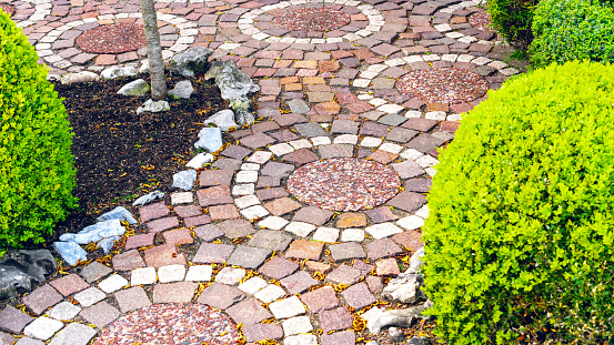 Circular paving of a path near the house and in the garden. An original variant of paving stones for garden paths. Red and white granite walkway laid out in a circular pattern. Creative paving example