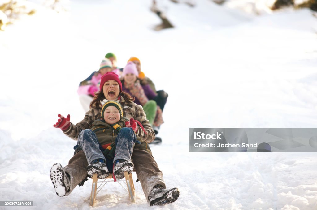 Mother and son (8-10) tobogganing in snow, family in background  Winter Stock Photo