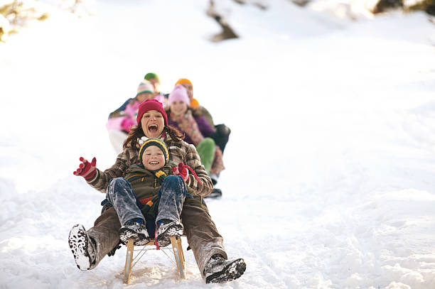 мать и сын (8-10) кататься на тобоггане в снегу, семья на фоне - winter стоковые фото и изображения