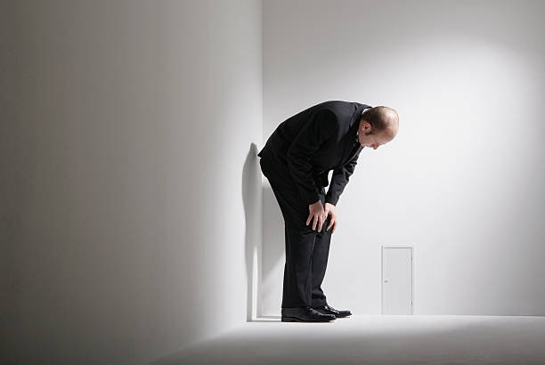 man crouching by small door in room - se courber en avant photos et images de collection