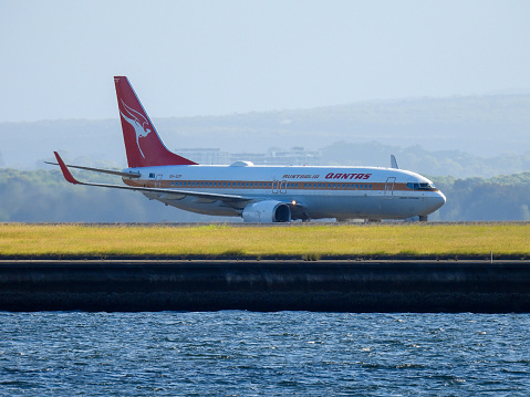 A Qantas Boeing B737-838 plane, registration VH-VXQ in Retro 1959 Livery, taxiing to the domestic terminal of Sydney Kingsford-Smith Airport after landing on the third runway as flight QF539 from Brisbane.  This image was taken from near the Port Botany Boat Ramp on a late sunny afternoon on 10 February 2024.