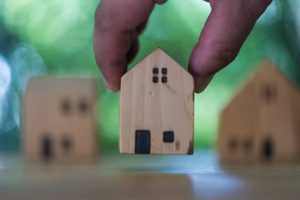 istock Hand choosing mini wood house model from model on wood table. 2004042667