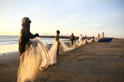 On the coast of Banda Aceh on 08/06/2019,  A group of fishermen from the Javanese village skillfully cleaned their nets. Amidst the sunset ambiance, they employed the traditional method of shore seine to catch fish. Their hands moved skillfully and systematically, clearing debris and repairing the nets. The twilight light enhanced their silhouettes, creating a beautiful portrayal of fishermen's lives deeply intertwined with the sea.
