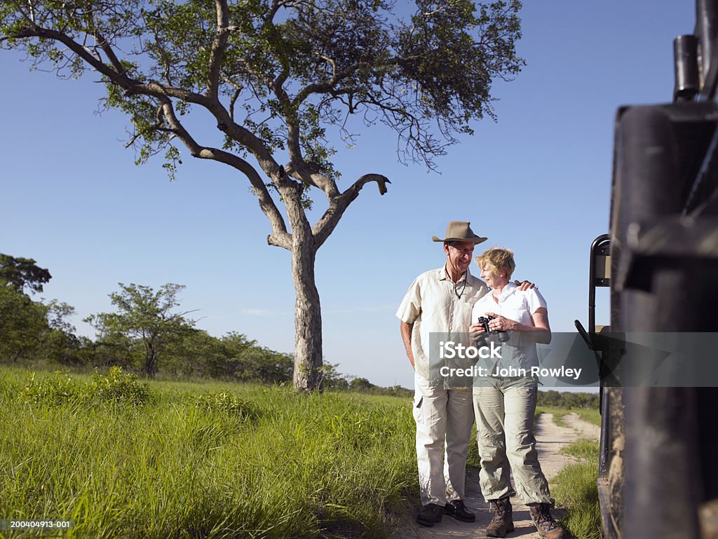 Couple by jeep, woman holding binoculars, man's arm around woman  Safari Stock Photo