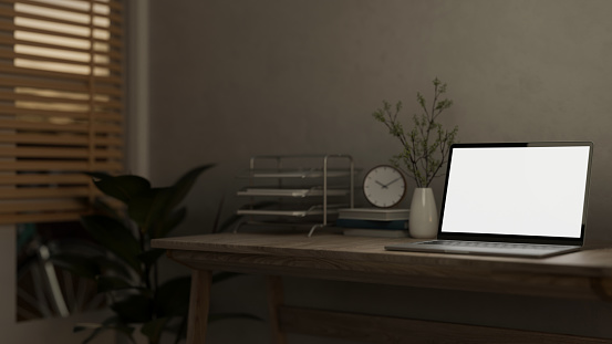 A white-screen laptop computer mockup and decor are placed on a hardwood desk in a minimally cozy home office. 3d render, 3d illustration