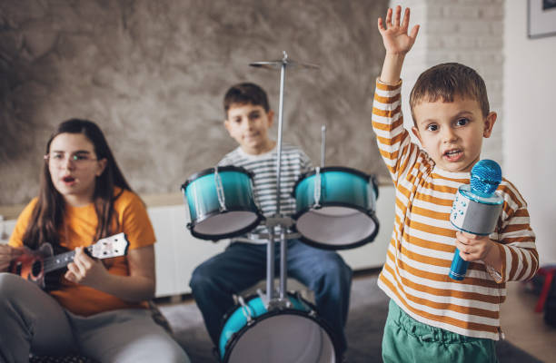 istock Portrait Of A Boy Singing Into A Microphone While Other Children Playing Instruments 2004114113