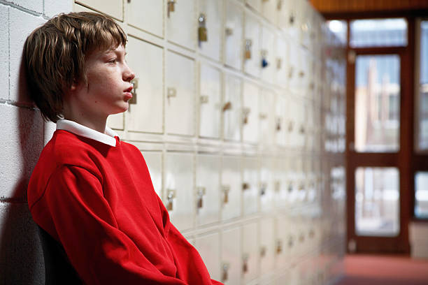 Schoolboy (11-13) sitting in corridor leaning head on wall, side view  punishment photos stock pictures, royalty-free photos & images