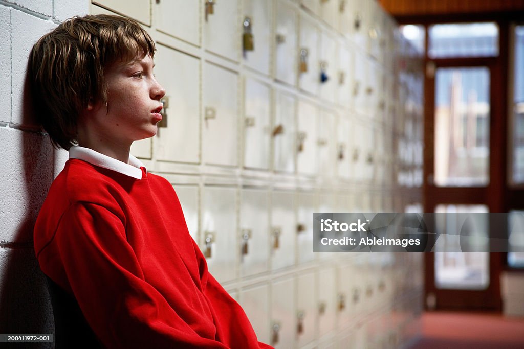 Schoolboy (de 11 a 13 anos) sentada no corredor cabeça inclinada na parede lateral - Foto de stock de Criança royalty-free