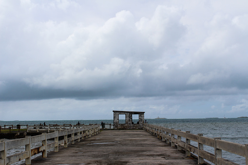 A wooden pier at the edge of the indian ocean. Small cabin at the end of the pier. Grey and cloudy skies, overcast and rain. Fishing area.