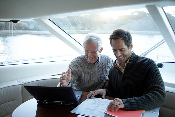 senior und älterer mann sitzt auf yacht mit laptop und lächeln - rushcutters bay stock-fotos und bilder