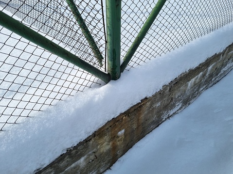 Snow-covered metal and concrete details of a street fencing structure