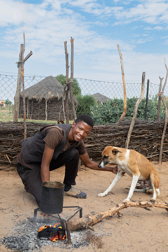 village african man, with his dog in the outdoors kitchen , cooking next to the fire