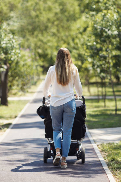 istock Young mom from back walking with twin baby stroller in green spring city park. Faceless active mother in casual clothes with double carriage for two child 2004280406