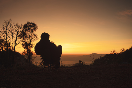 landscape and travel concept with solo freelancer man sit on chair and see sunrise with layer of mountain background