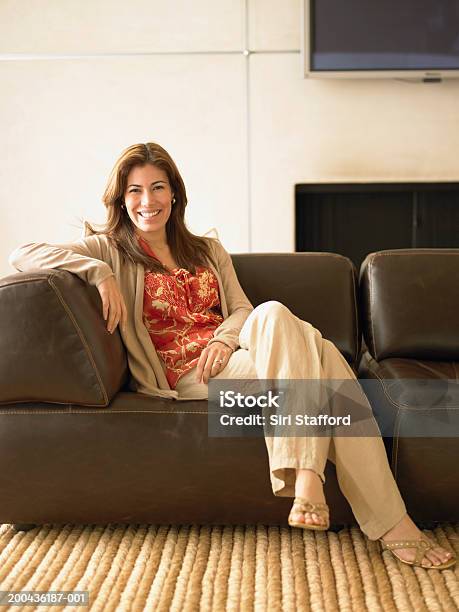 Woman Sitting On Sofa In Living Room Portrait Stock Photo - Download Image Now - Cardigan Sweater, Happiness, Indoors