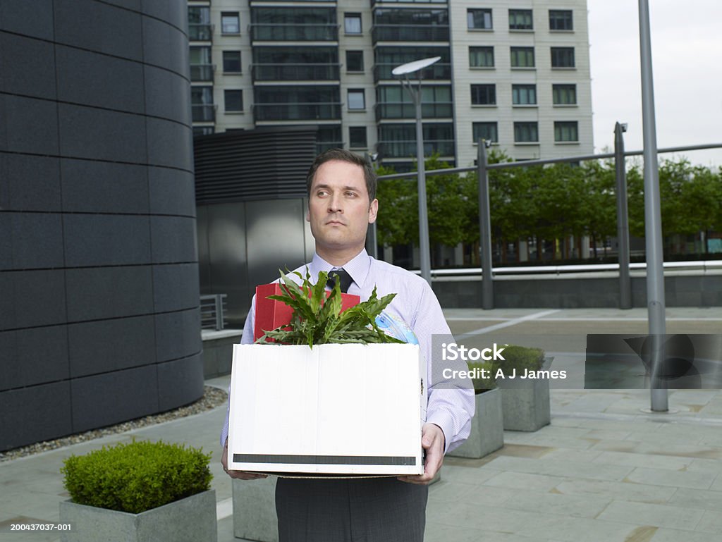 Businessman carrying box containing plant and files on street London, UK. Rejection Stock Photo