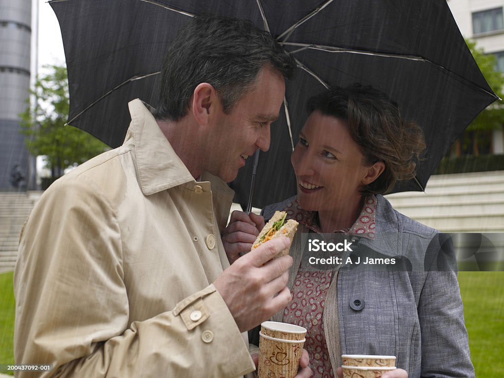 Hombre y mujer compartir una sombrilla mientras almuerza, smili - Foto de stock de Lluvia libre de derechos