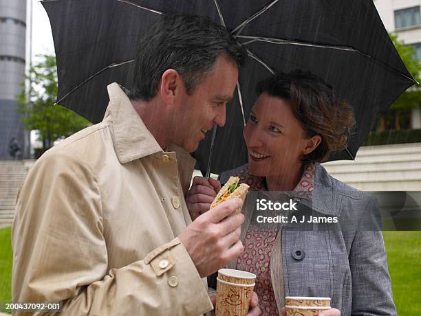 Hombre Y Mujer Compartir Una Sombrilla Mientras Almuerza Smili Foto de stock y más banco de imágenes de Lluvia