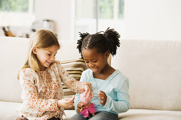 two girls (4-6) playing with doll in living room, smiling - little girls only fotografías e imágenes de stock