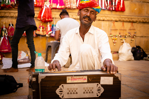 Jaisalmer, Rajasthan, India - October 30th 2023: Portrait of a Rajasthani male street singer wearing traditional turban singing with harmonium on colorful background