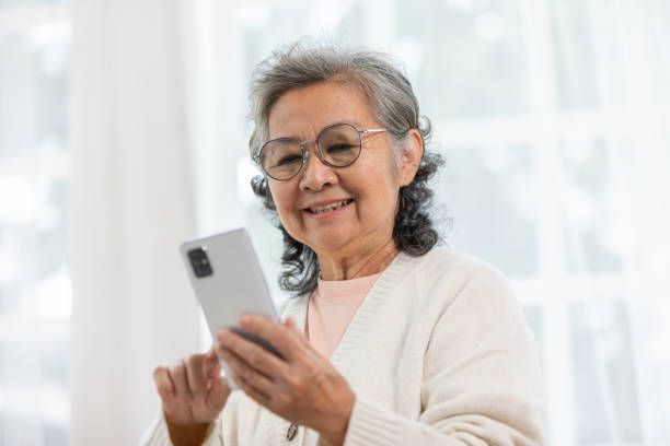 istock Happiness beautiful elderly asian woman with white hairs sitting on sofa using mobile phone and social media smile in cozy living room at home,Senior Wellness lifestyle at home concept 2004379577