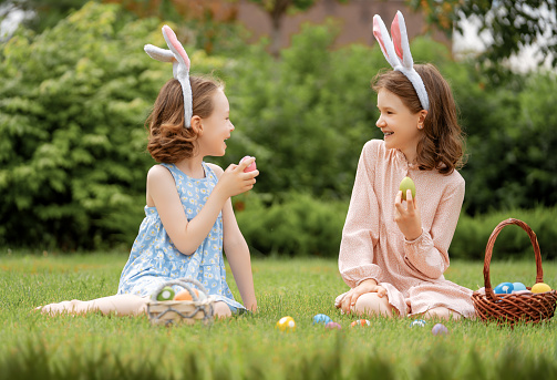 Beautiful children with painting eggs outdoors. Happy family celebrating Easter in nature. Cute little girls are wearing bunny ears.