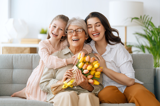 Happy mother's day. Child daughter and mother are congratulating granny giving her flowers tulips. Grandma, mum and girl smiling and hugging. Family holiday and togetherness.