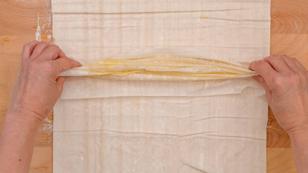 istock Phyllo daugh pastry filled with cream cheese   recipe. Woman hands roll buttered dough layers, close-up baking process 2004403238