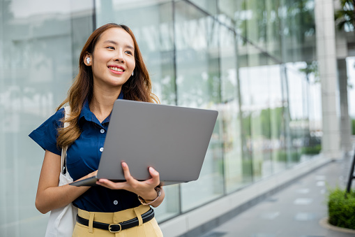 Young woman sitting on the steps with her laptop and cell phone, wearing bluetooth earbuds, enjoying the outdoors and being productive at work.