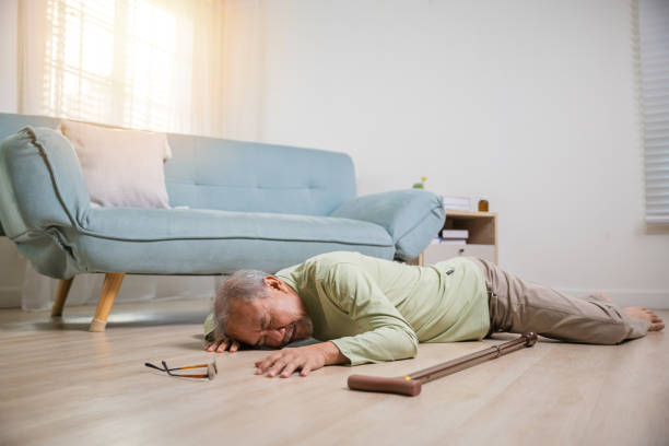 Elder man falling on the floor alone with walking stick on living room at home - foto stock