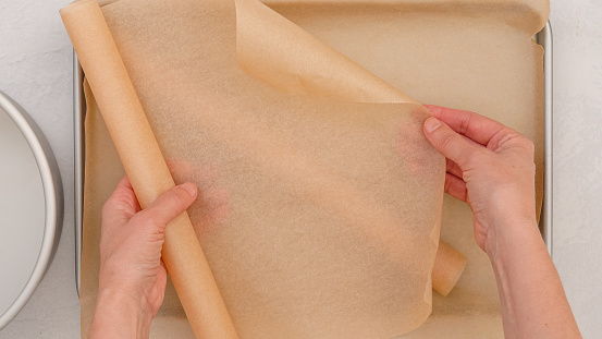 Close-up depiction of the baking process, a woman's hands delicately place parchment paper on a baking pan, showcasing meticulous preparation and attention to detail.