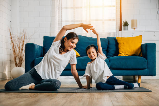 A mother and her little daughter practice yoga together focusing on relaxation and balance in the cozy living room - foto stock