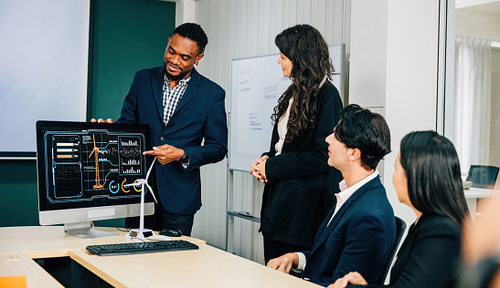Colleagues with diverse skills and backgrounds convene at the office, discussing new investment strategies on a PC computer monitor. Their teamwork, discussion, and leadership foster marketing success