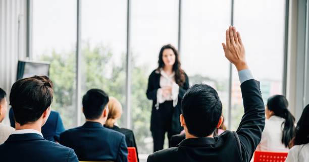 istock One individual among a group raises a hand in a conference demonstrating active participation teamwork and a willingness to engage in discussions. 2004409780