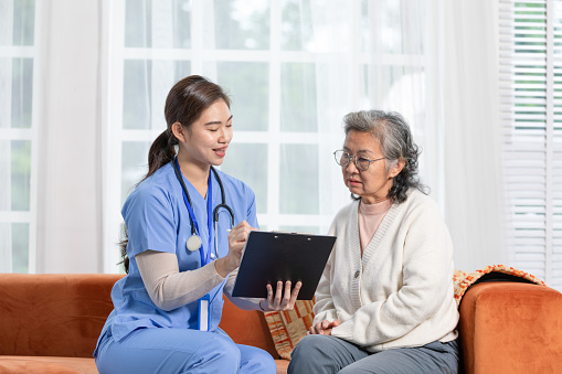 Asian female doctor who works in office and consults to patient explains health care symptoms and help elderly woman, give medicines. Writing down diagnosed and symptoms, elderly care, health care