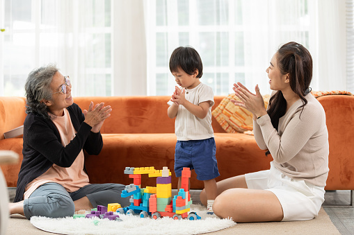 Heartwarming scene as baby toddler enthusiastically plays with stacking blocks, bringing joy to the faces of both their loving grandmother and mother in delightful family bonding moment. love concept