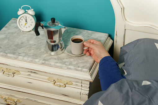 woman lying in bed having a cup of coffee for breakfast upon waking up