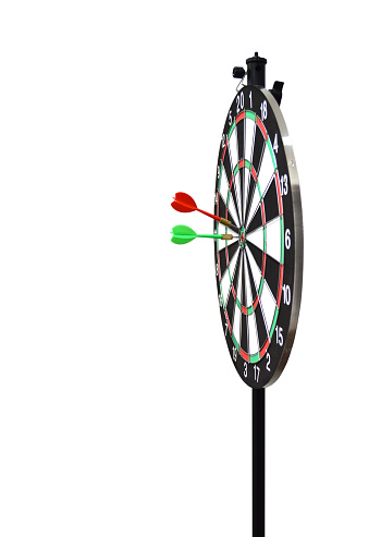 Cutout of side view of two darts or arrows on target, one red and other green hitting bull's eye spot on in inner circle of circular  dartboard isolated over vertical white background denoting success, win, achievement of business target, competition